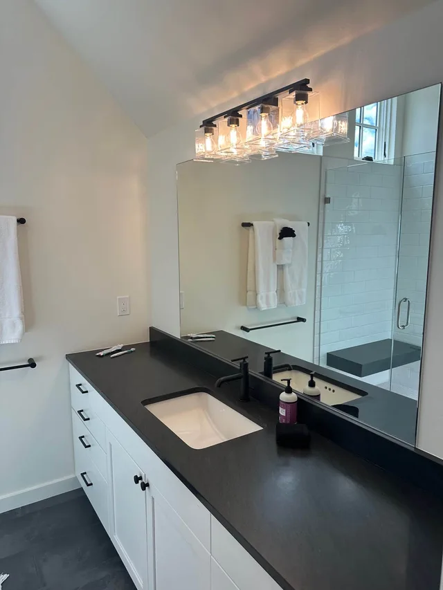 En-suite bath with a double vanity, black-stone counter, and walk-in shower