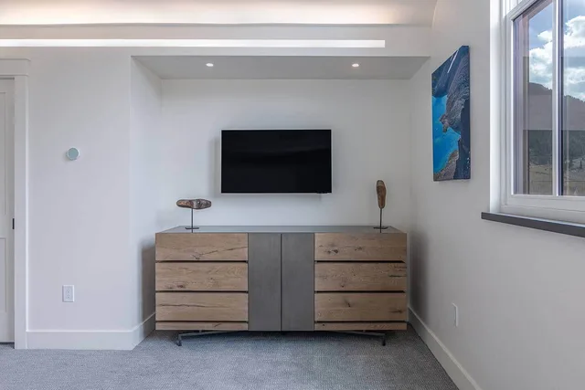 Guest bedroom with an oak dresser, wall-mounted TV, and mountain art